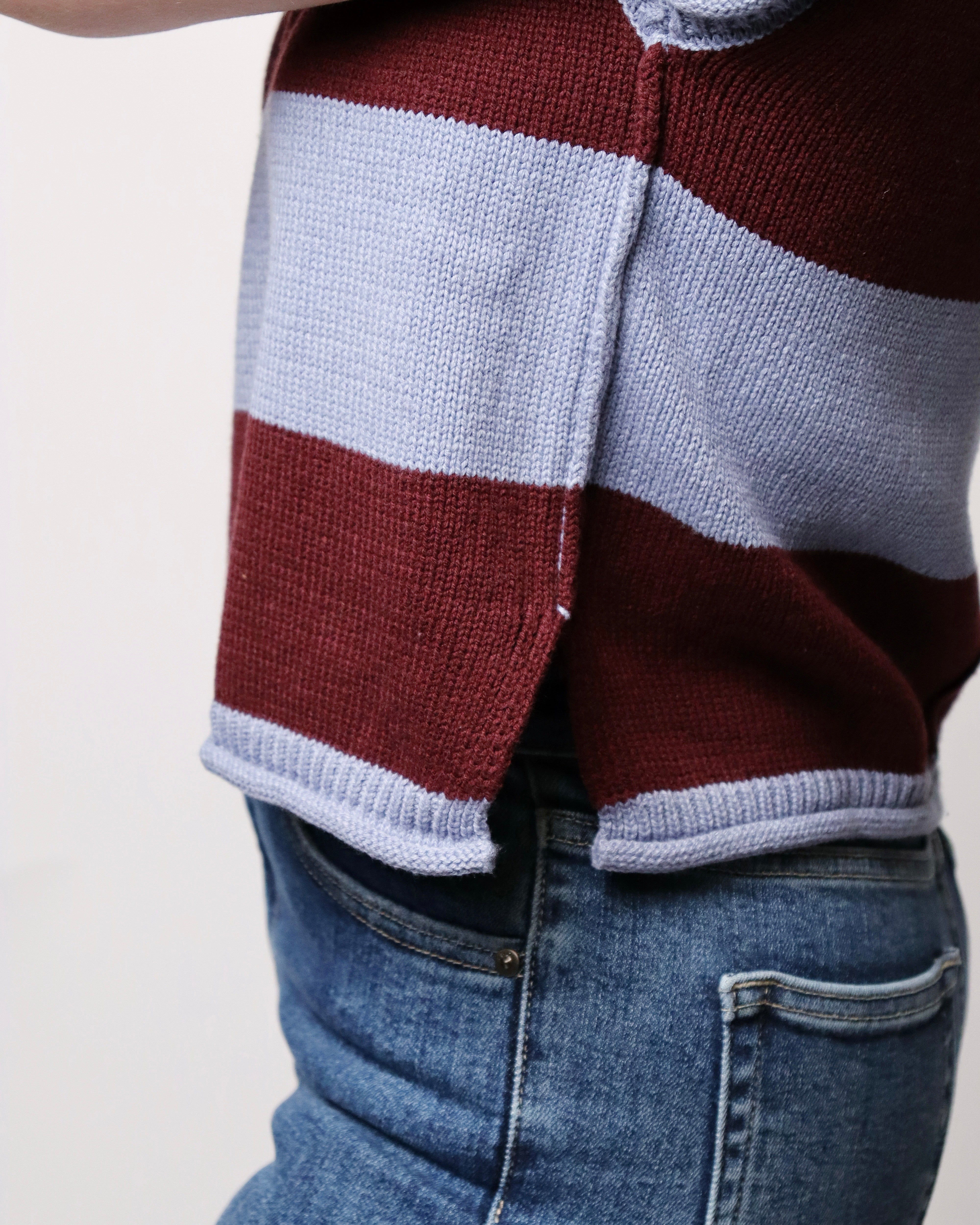 Close-up of a person wearing a striped knit sweater with horizontal bands of burgundy and light gray, paired with blue jeans.