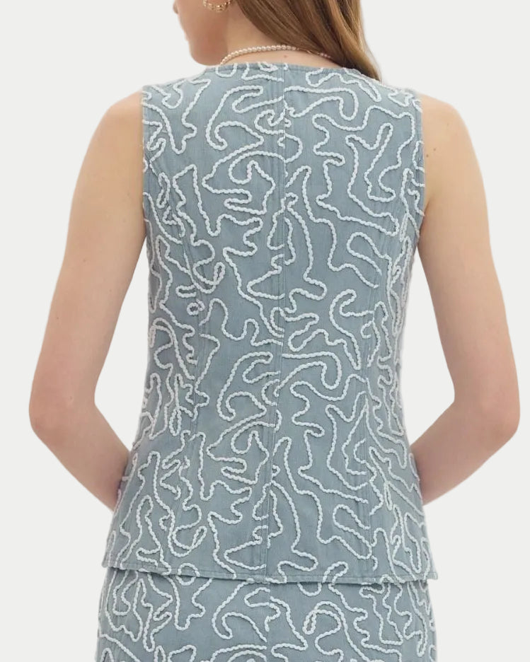 Woman wearing a sleeveless light blue embroidered vest top.  Button front. Silver buttons.  Fitted silhouette.  Neutral background back view