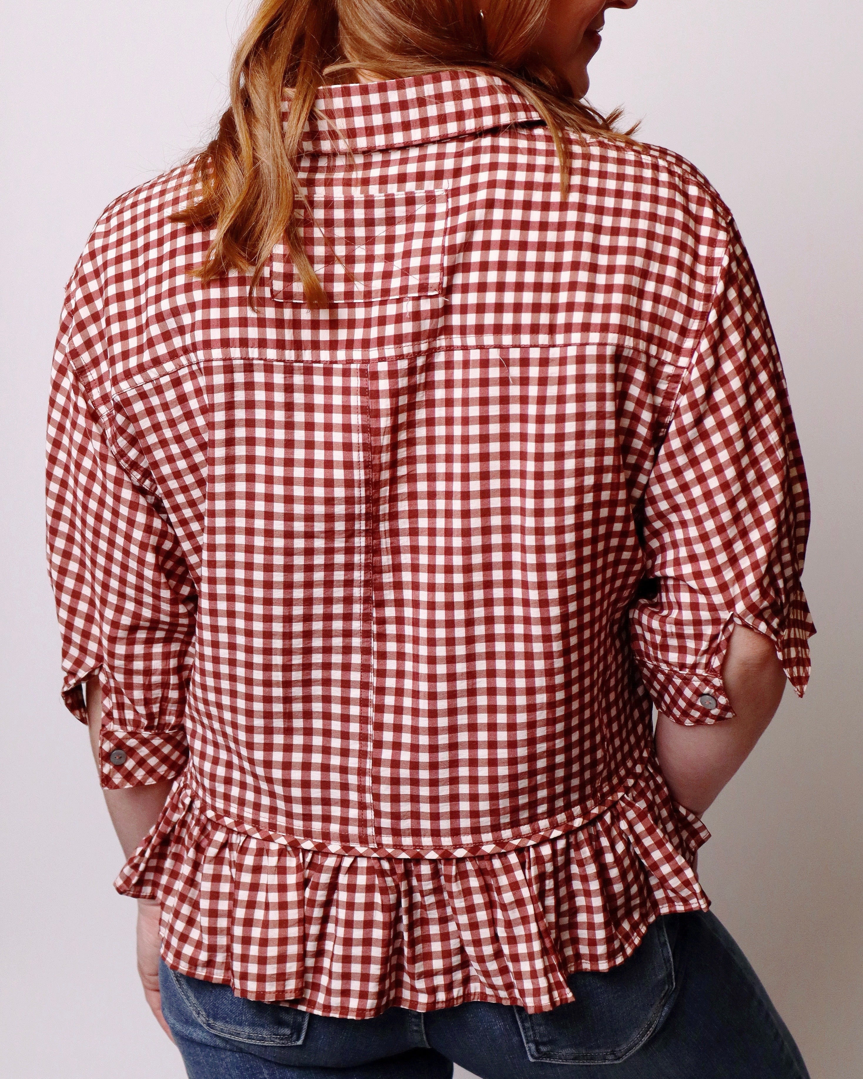 A woman wearing a red and white gingham check short-sleeve blouse with a ruffled hem, shown from the back against a plain light background.