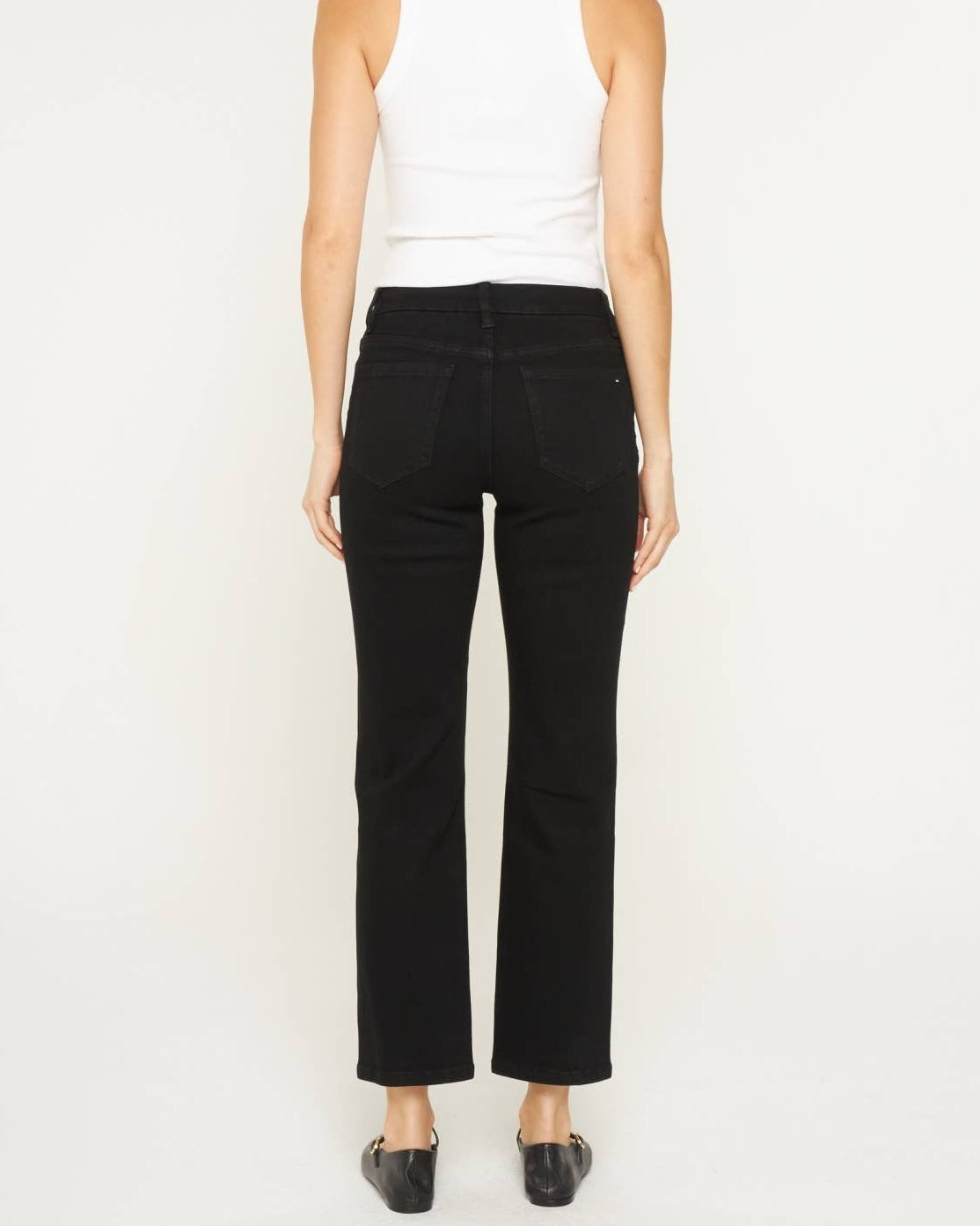 Model wearing black ankle length denim.  Mid rise.  on a neutral background. back view