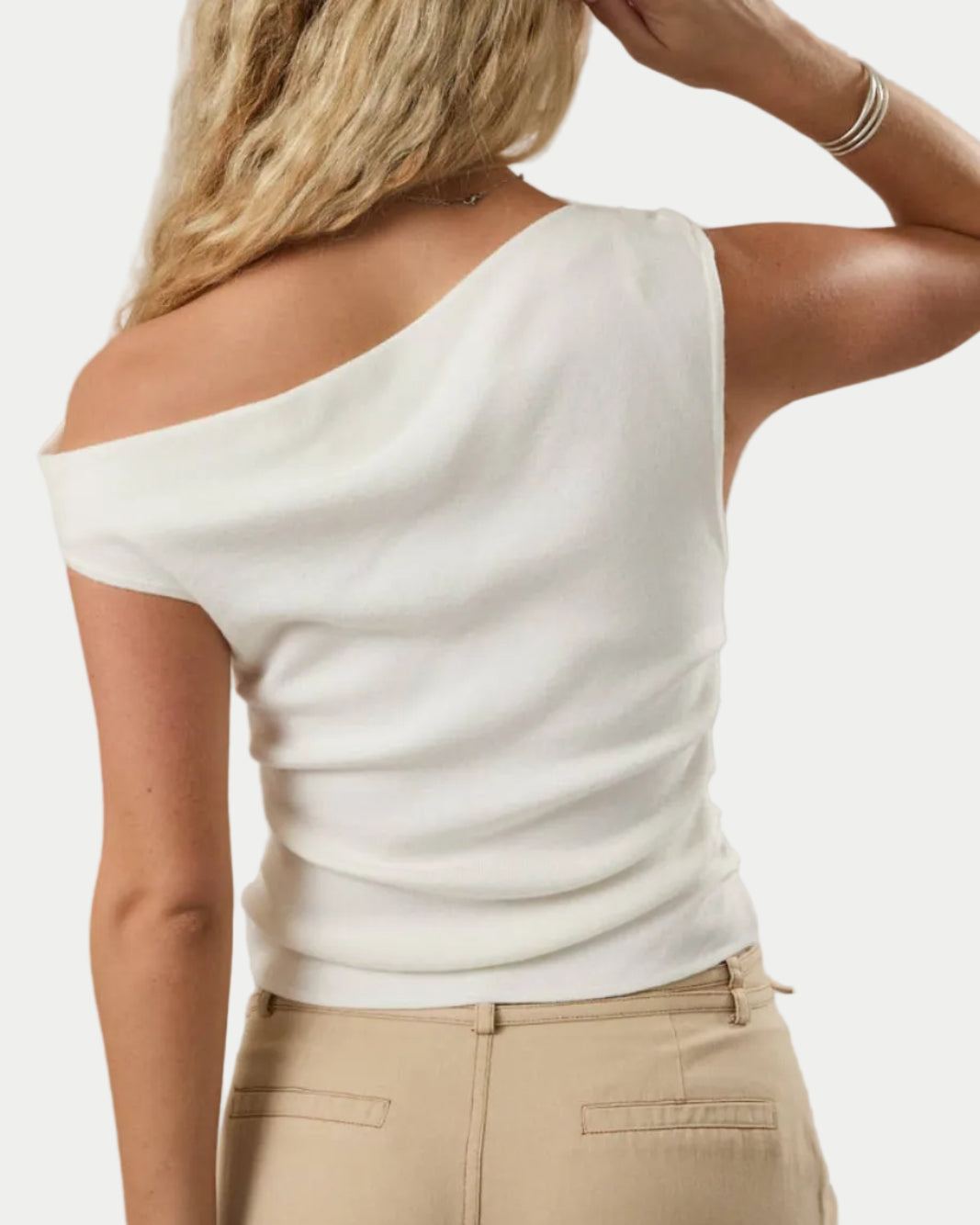 Woman wearing a white off-shoulder top and beige pants against a neutral background