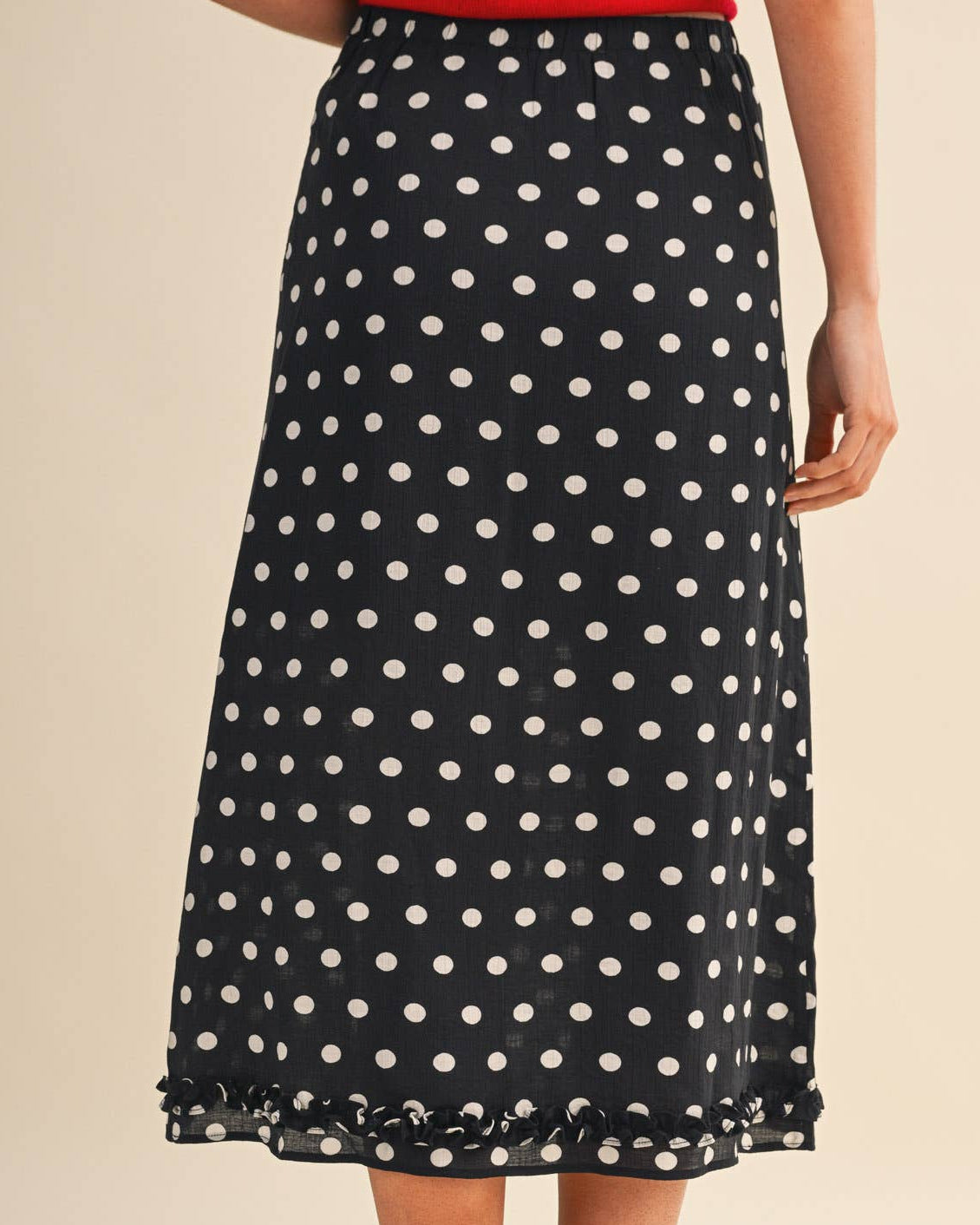 Model wearing a black polka dot skirt on a neutral background back view