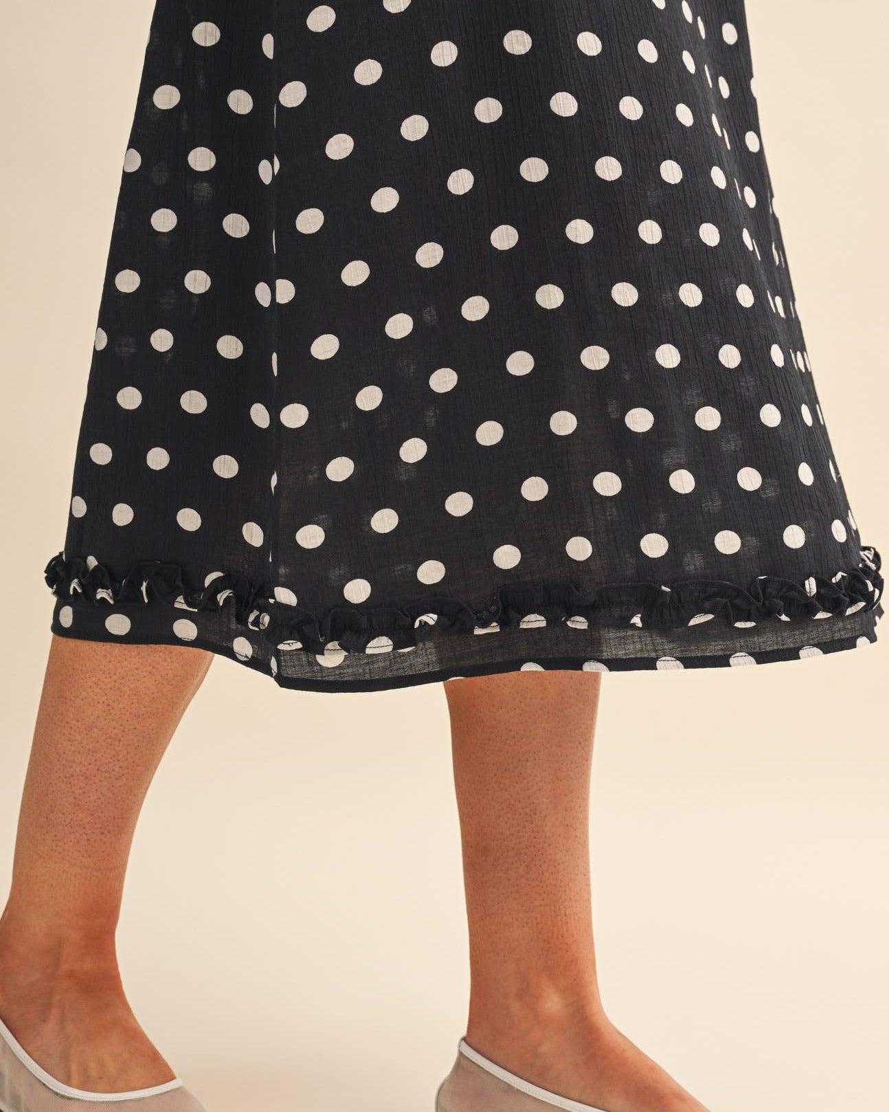 Model wearing a black polka dot skirt on a neutral background close up view