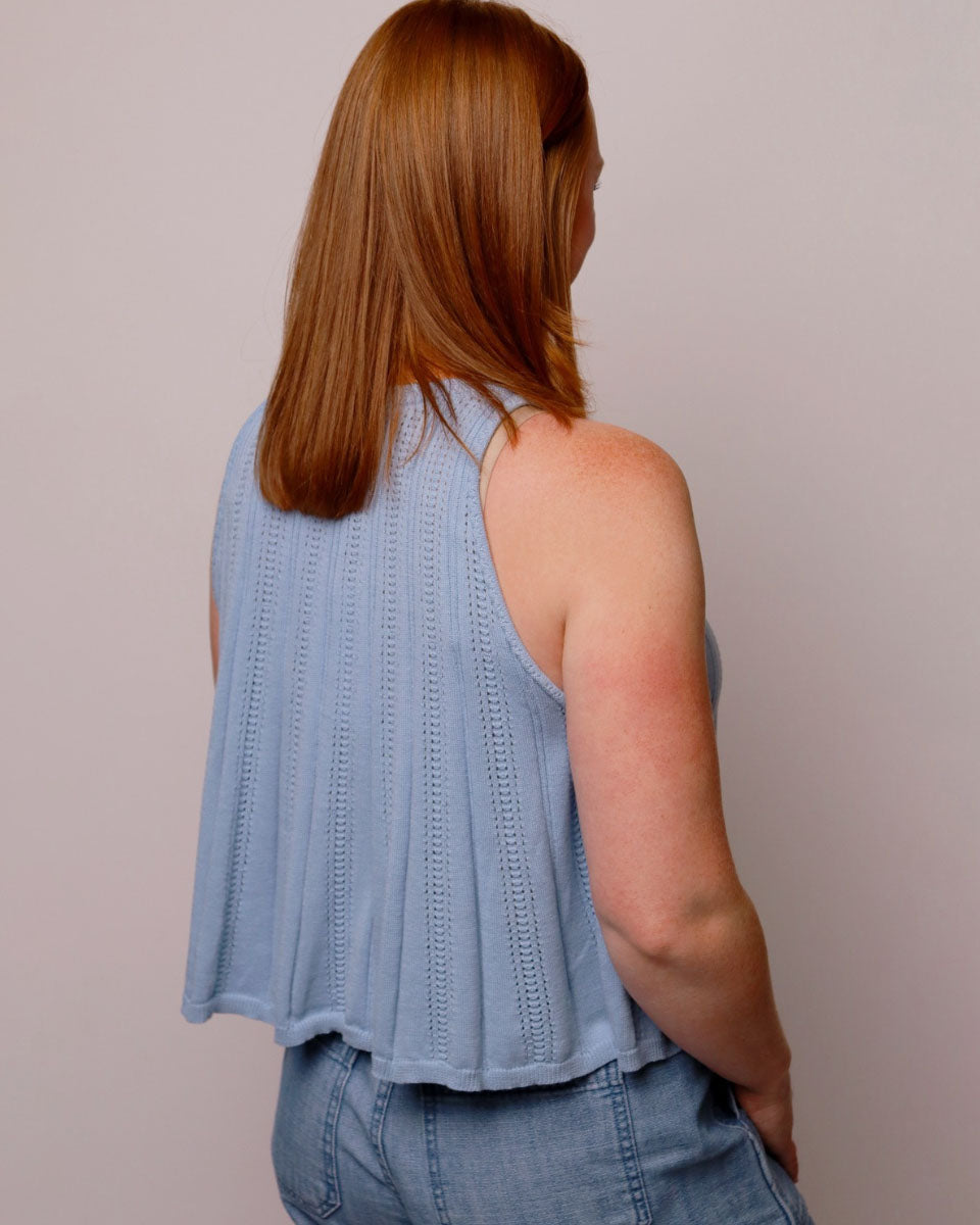 Woman wearing a light blue sleeveless top and shorts against a plain background