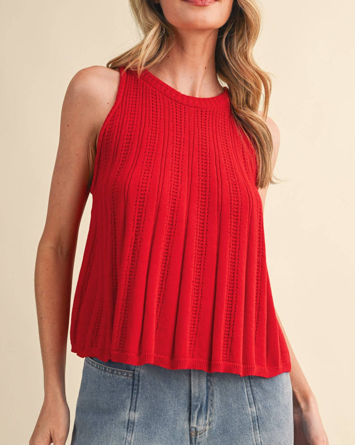 Woman wearing a red sleeveless top and blue jeans on a beige background
