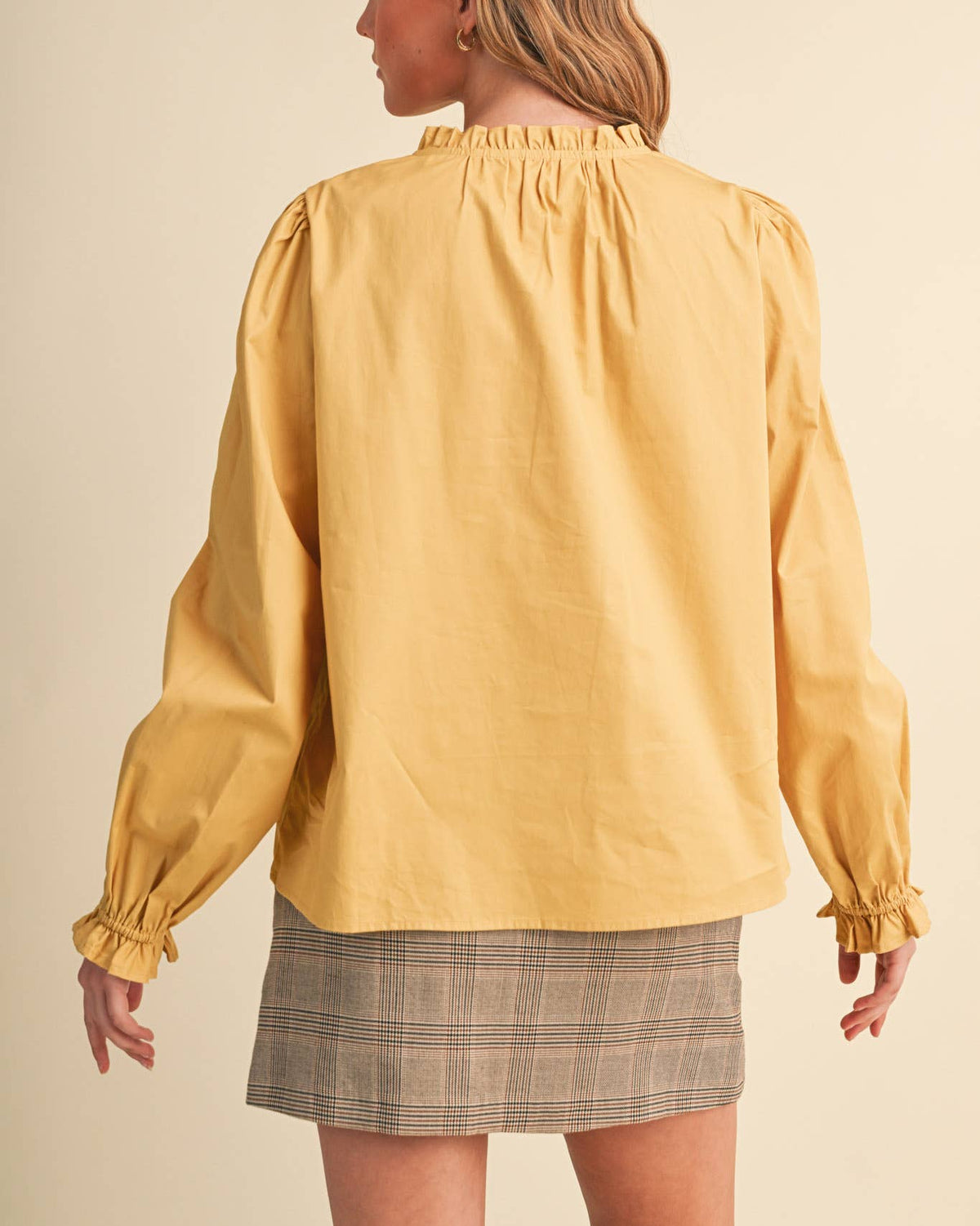 A woman wearing a honey gold long sleeve button up blouse with lace details on a neutral background .