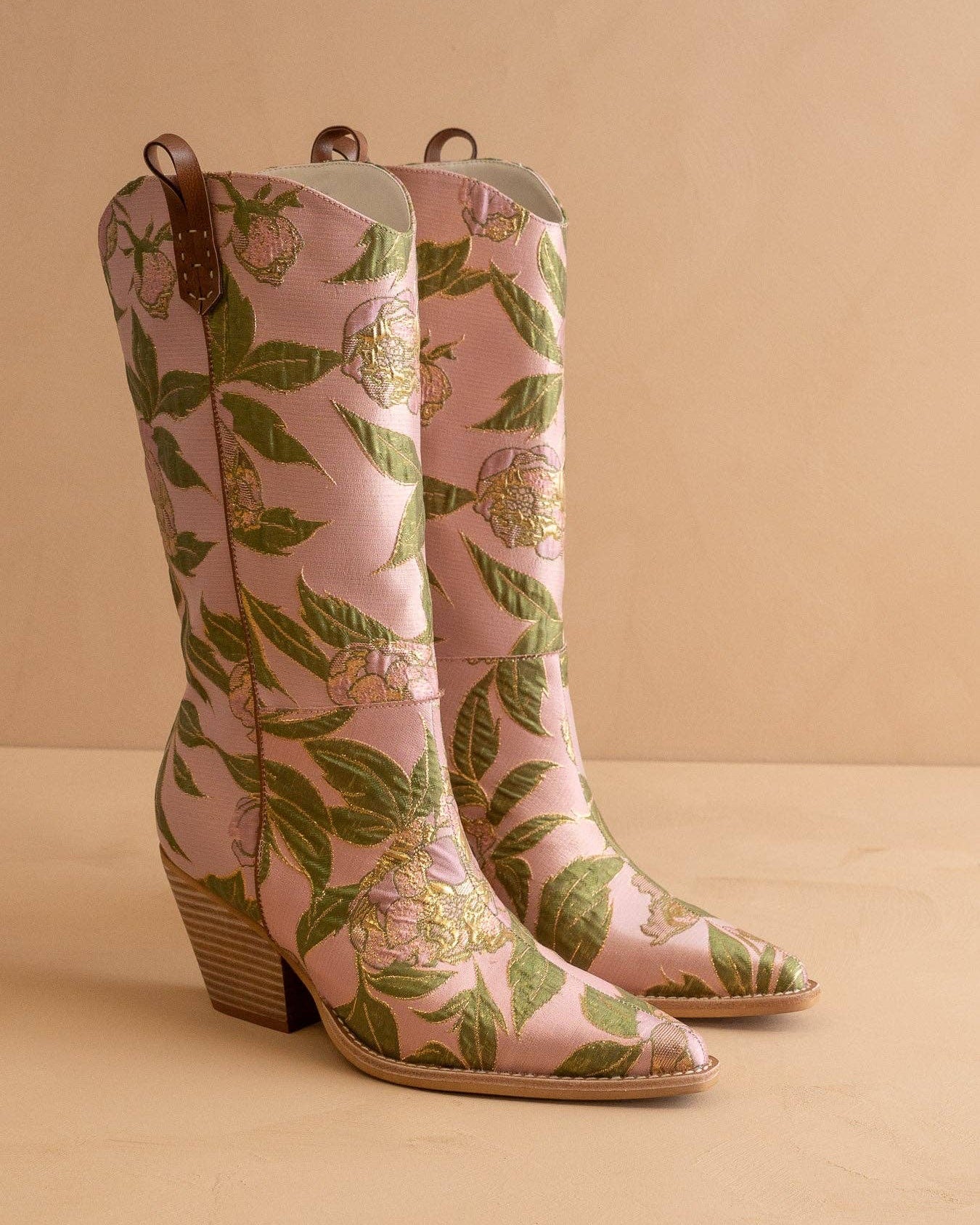 Pink floral-patterned cowboy boots on a beige background