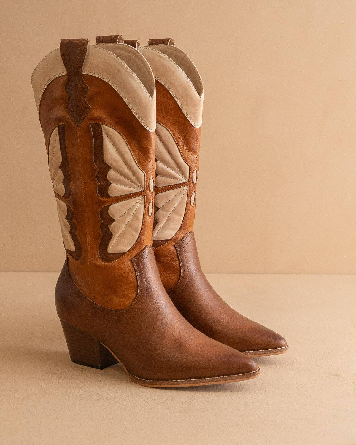 Pair of brown and beige cowboy boots on a beige background
