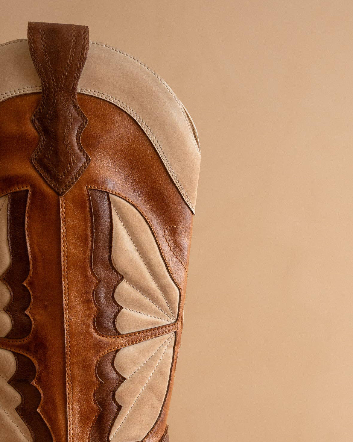 Close-up of a brown and beige leather boot with decorative patterns on a beige background