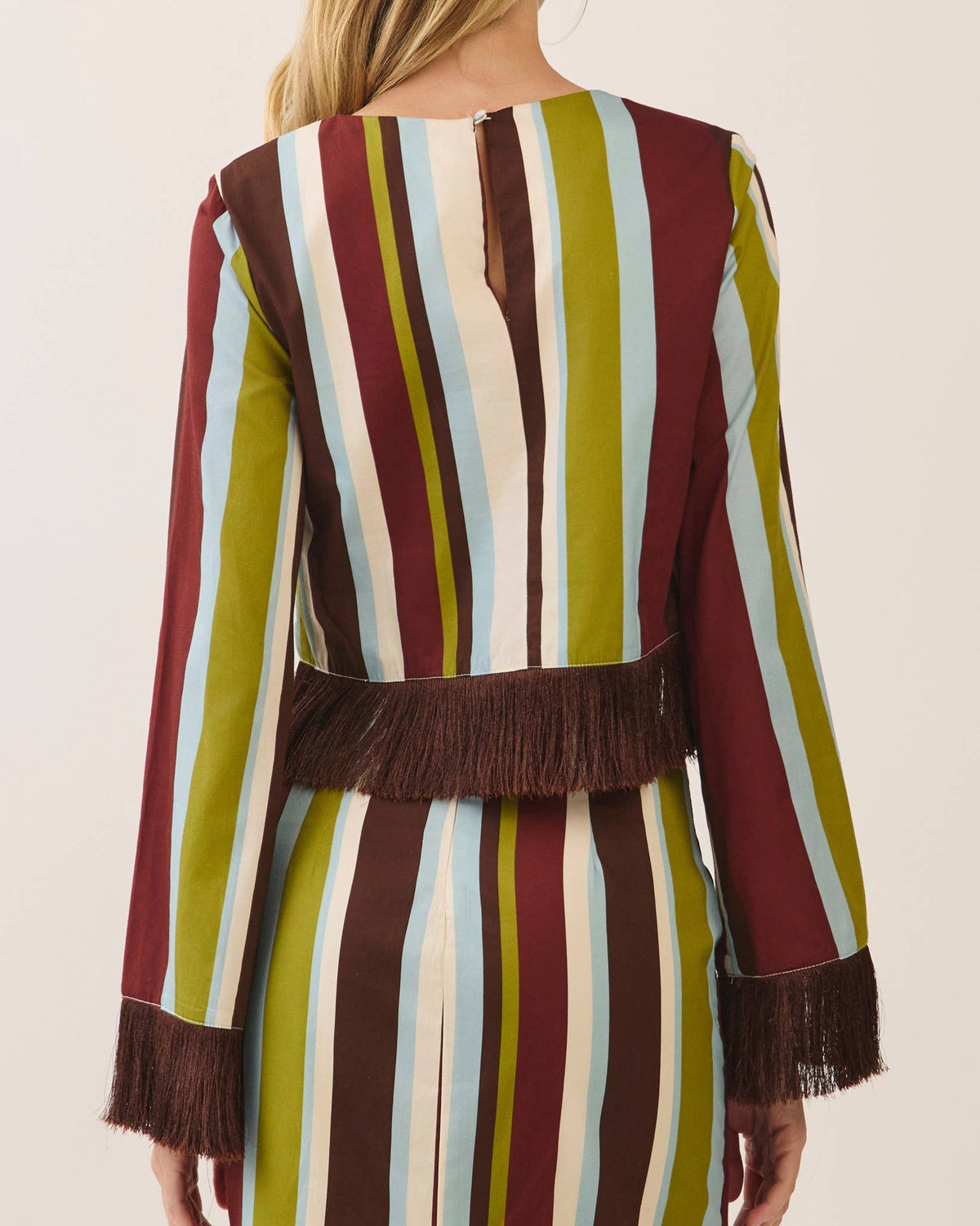 Model wearing a vertical striped long sleeve blouse with fringe at the cuff and hem on a neutral background.