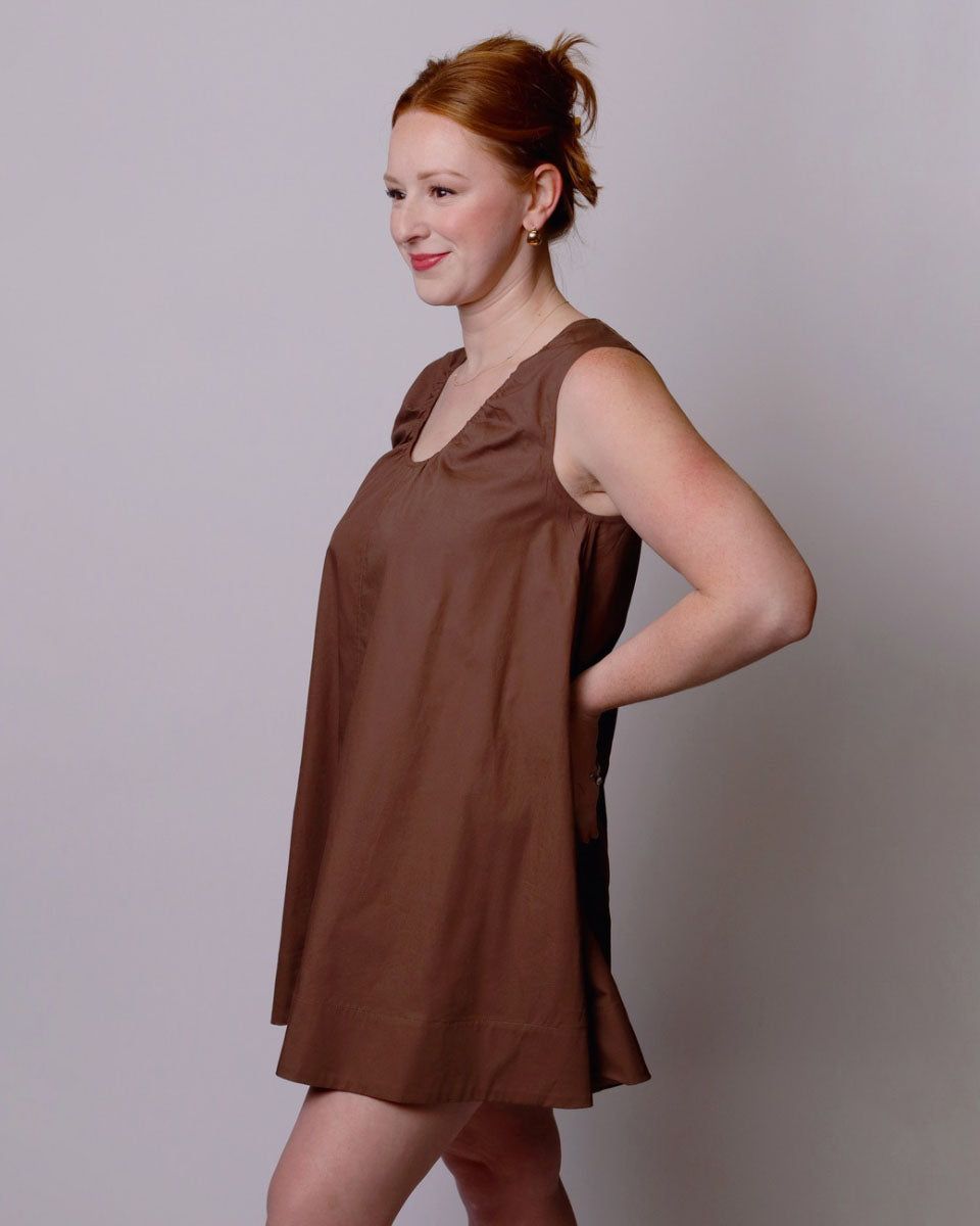 Woman wearing a brown sleeveless dress against a plain background