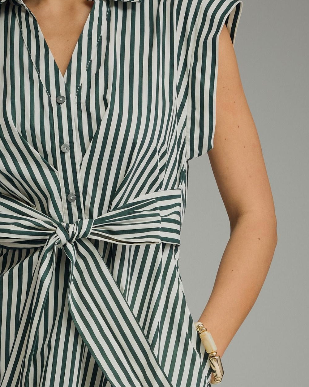A woman modeling a capsleeve midi dress with vertical green and white stripes, a collared neckline, and a self-tie waist, photographed against a neutral studio background. close up