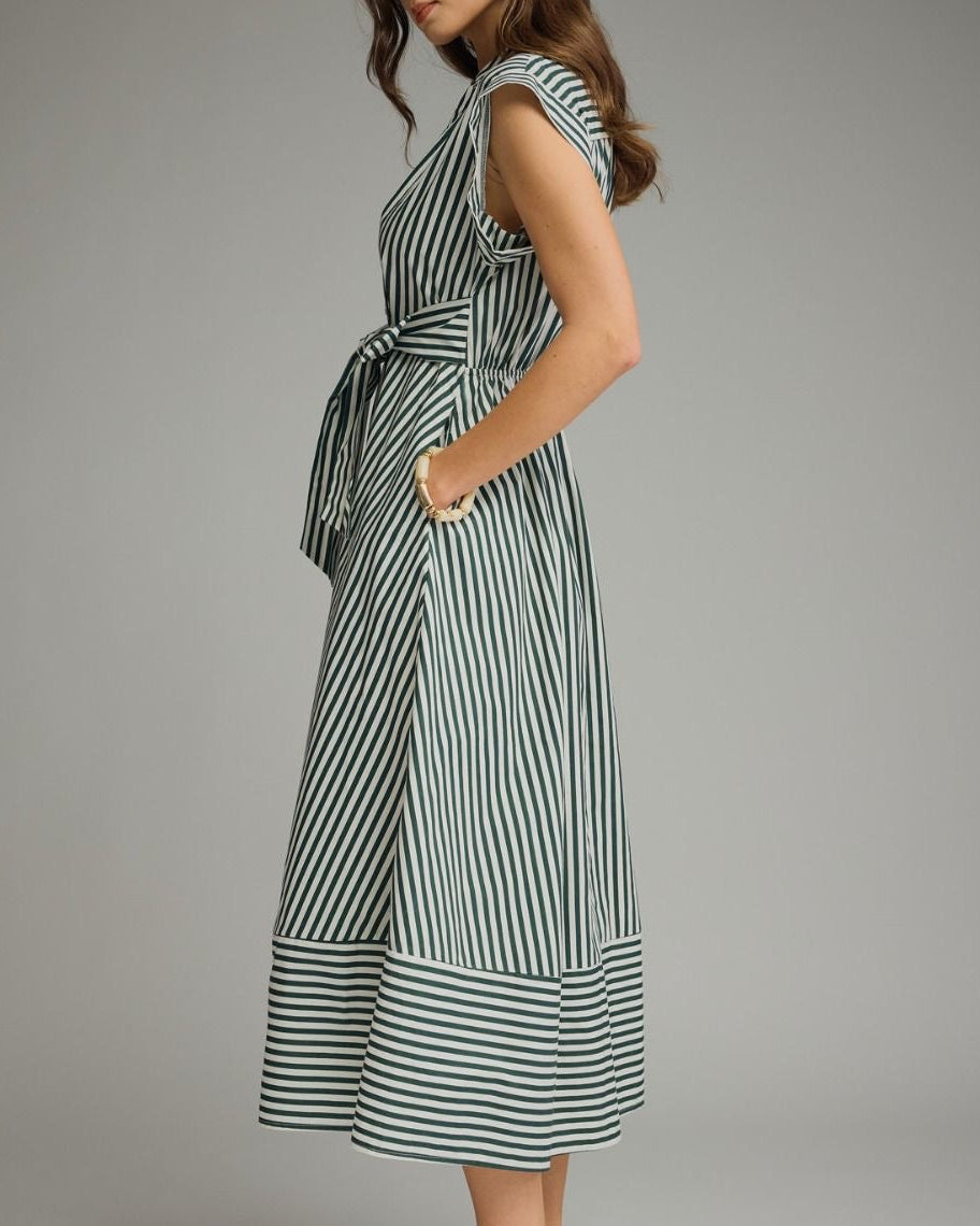 A woman modeling a capsleeve midi dress with vertical green and white stripes, a collared neckline, and a self-tie waist, photographed against a neutral studio background. side view