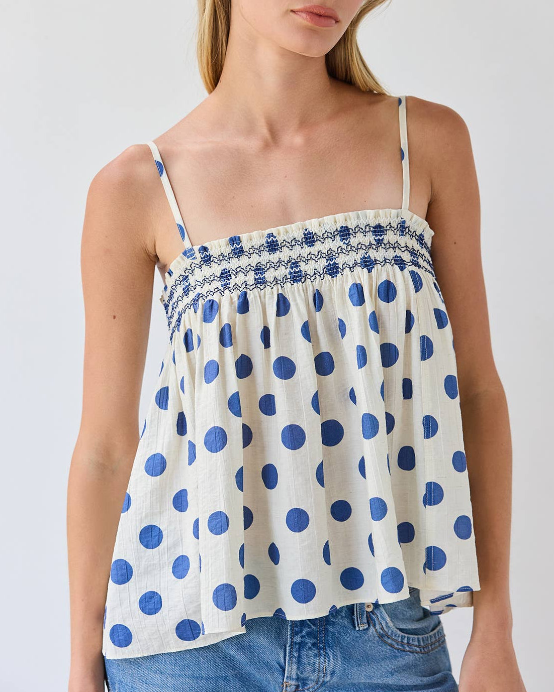 Model wearing a white tank top with blue polka dots on a neutral background