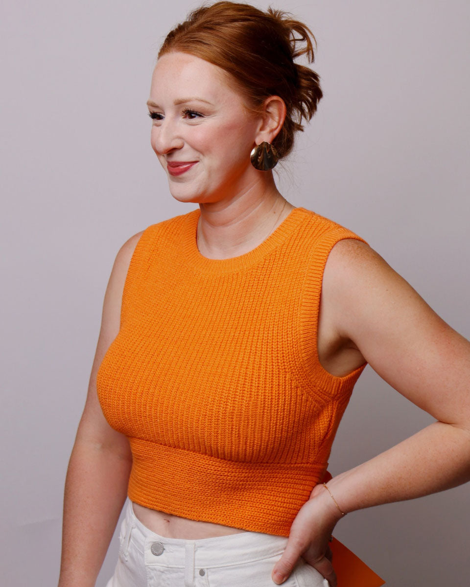 Woman wearing an orange sleeveless top against a plain background