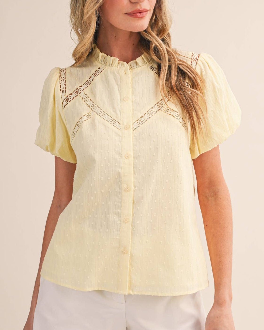 Woman wearing a light yellow blouse with lace details and white shorts on a beige background