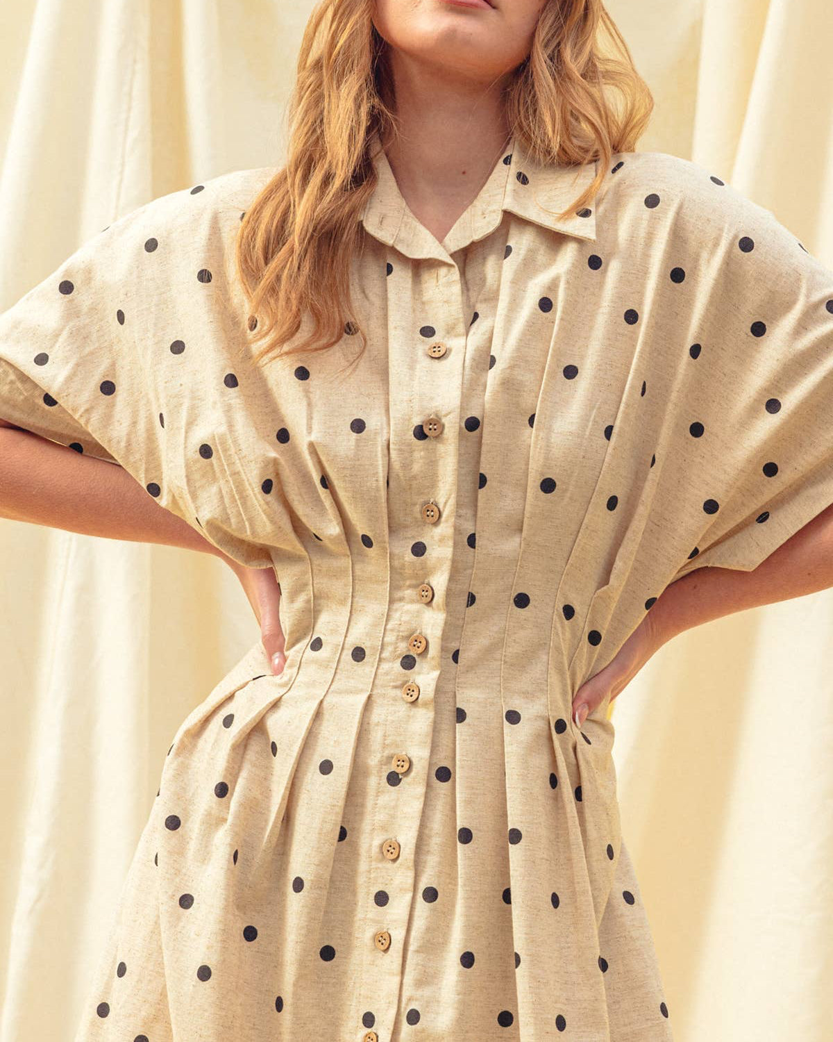Woman wearing a beige dress with black polka dots against a neutral background