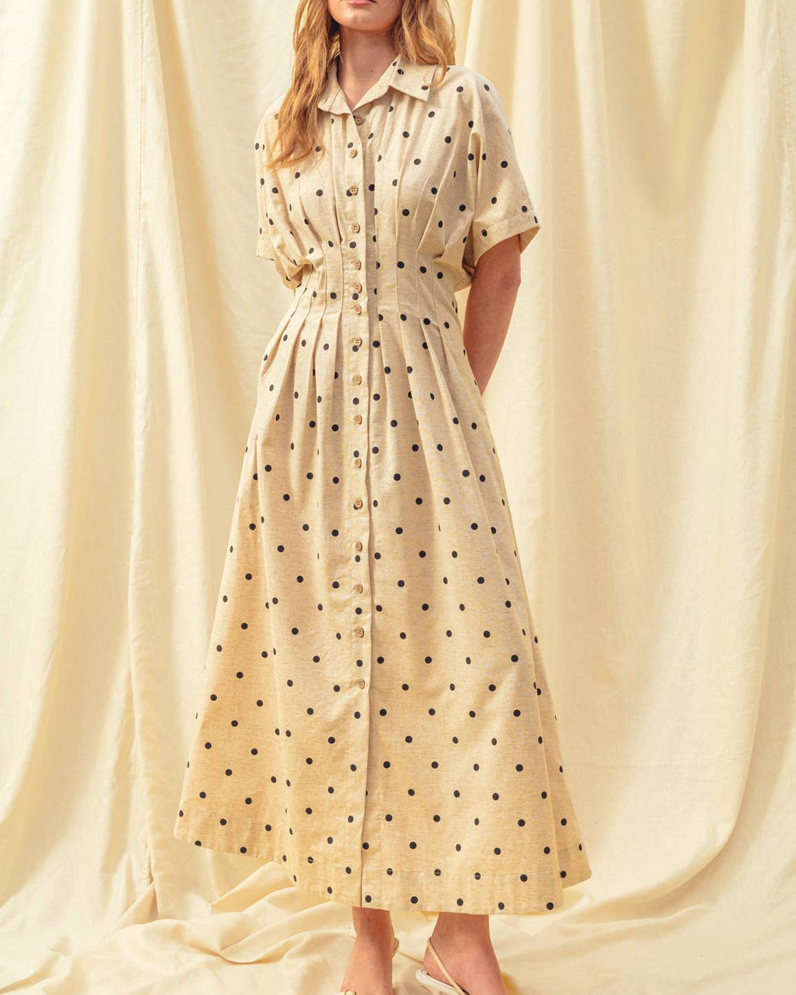 Woman wearing a polka dot dress standing against a draped fabric background