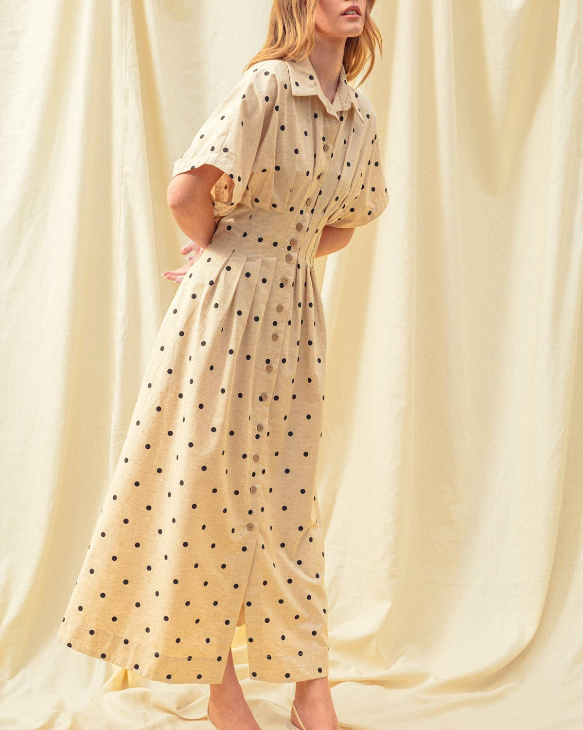 Woman wearing a polka dot dress against a beige curtain background