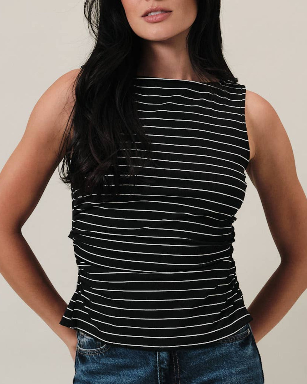 Model wearing a black and white striped tank top with ruching on the sides on a neutral background