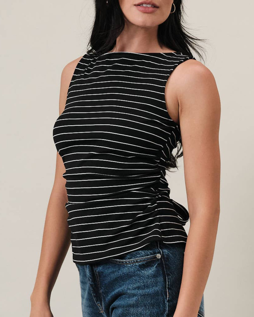 Model wearing a black and white striped tank top with ruching on the sides on a neutral background