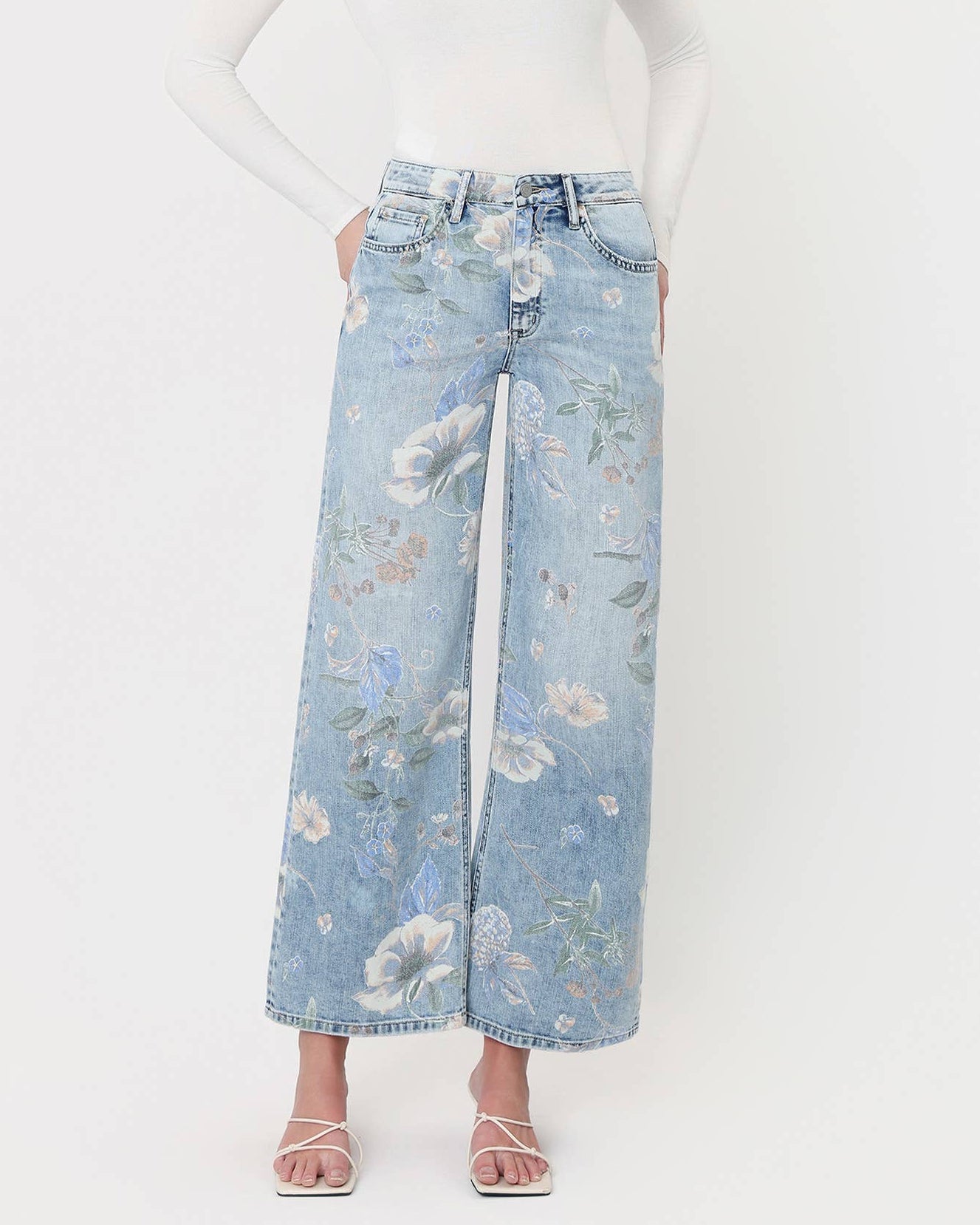 Woman wearing a white long-sleeve top and floral denim pants on a white background
