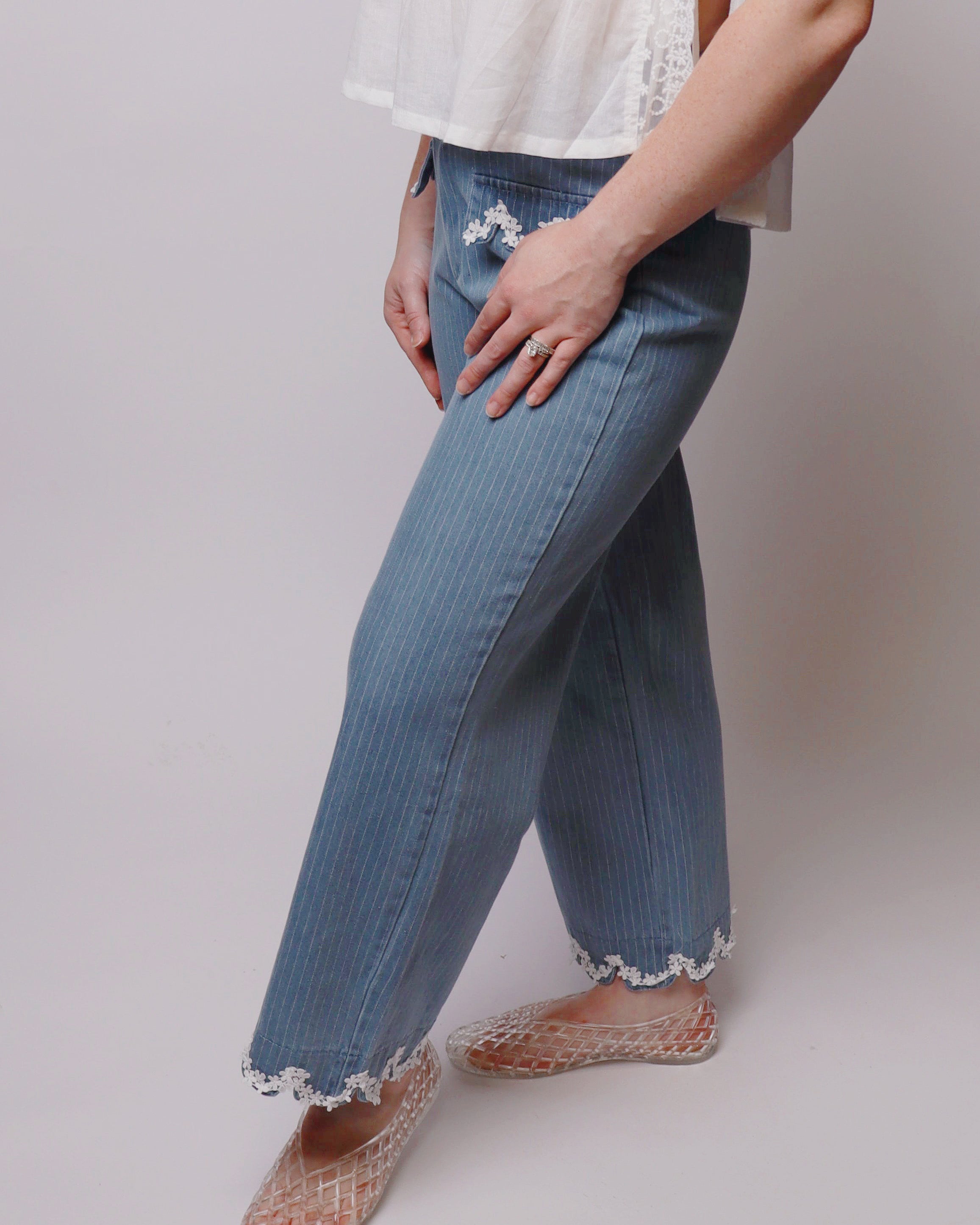 Person wearing blue jeans with lace trim on a plain background