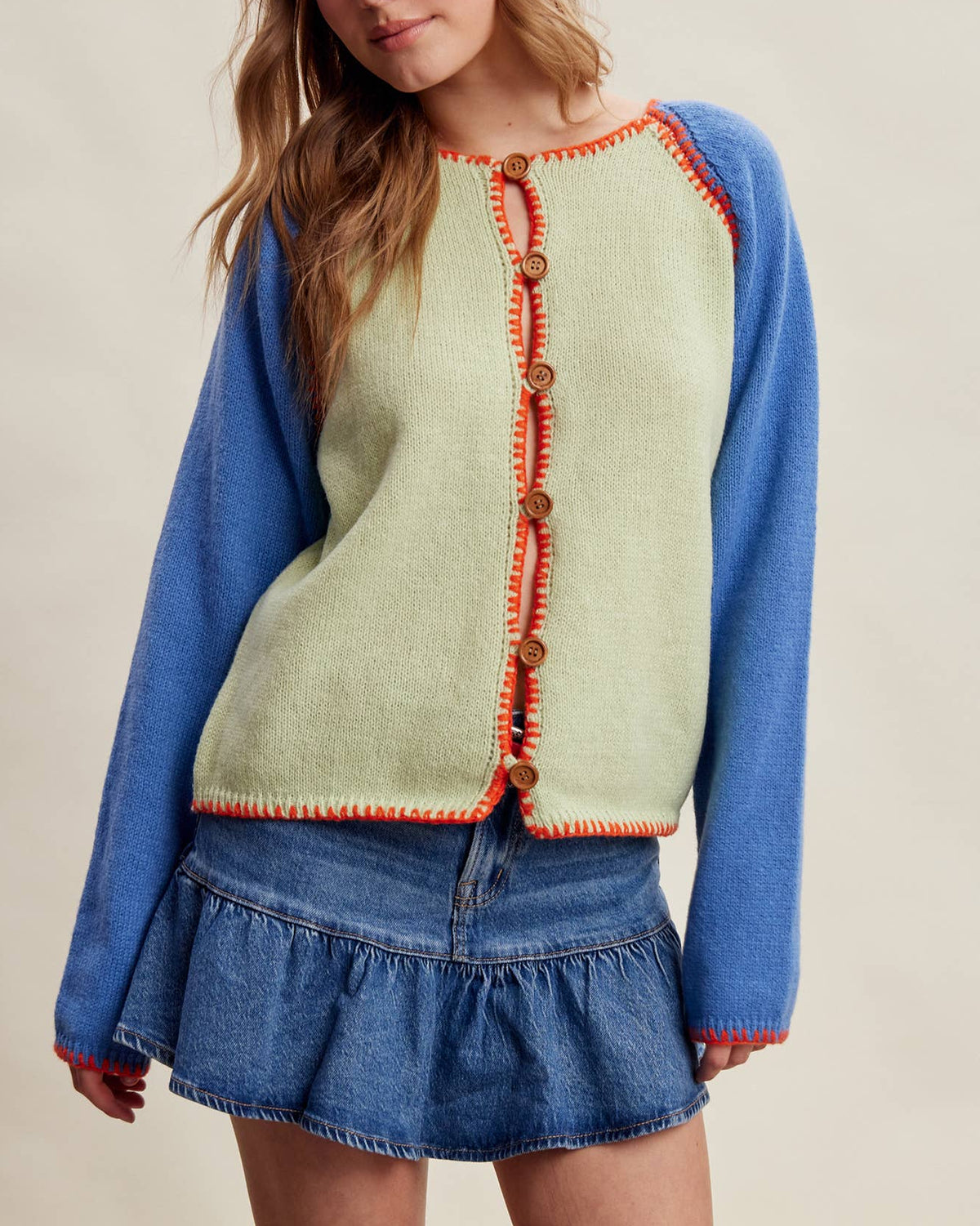 Model wearing a green melon cardigan with blue sleeves and orange stitching on a neutral background.
