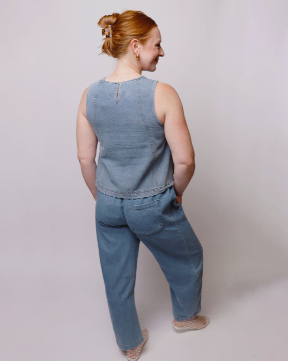 Woman wearing a blue denim sleeveless top and pants against a plain background