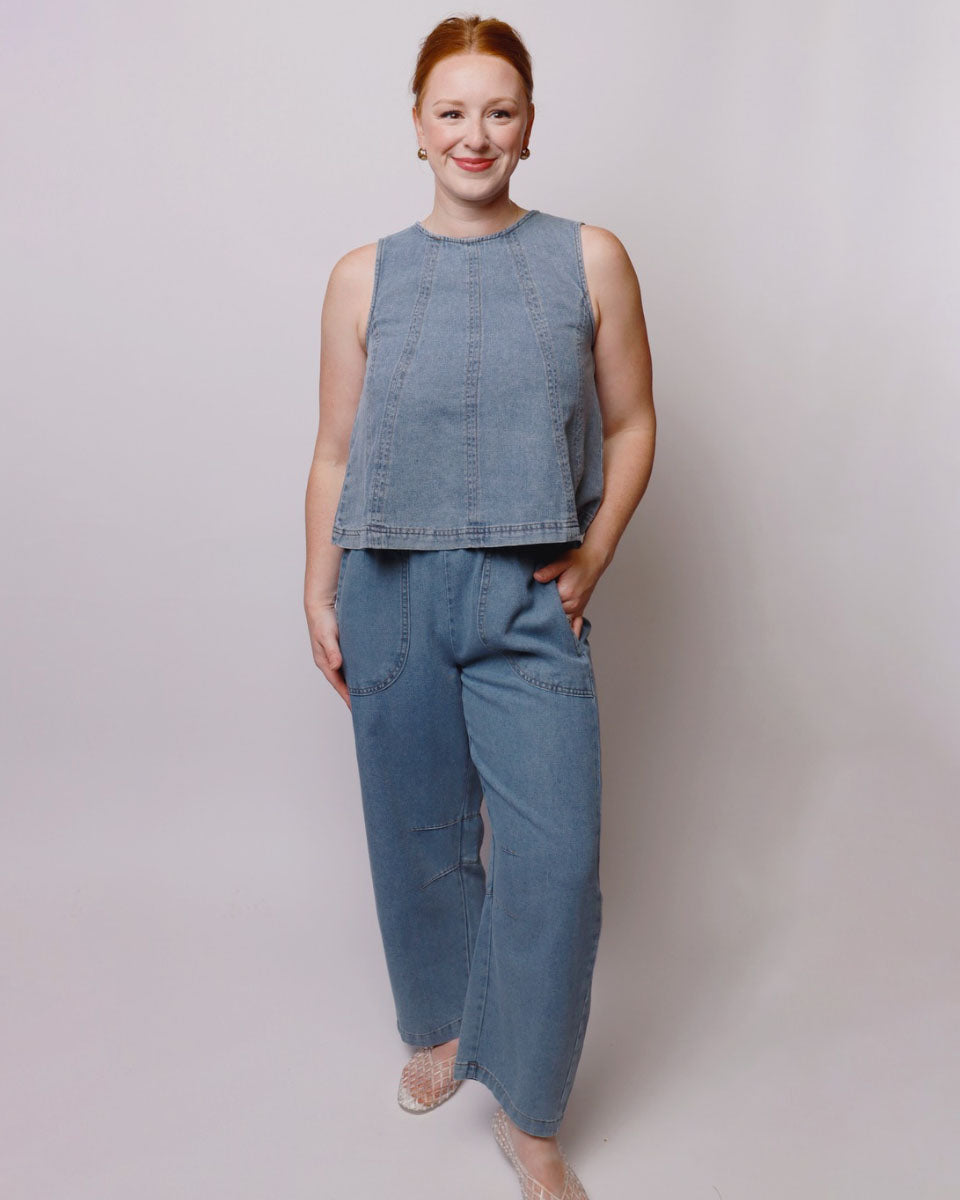 Woman wearing a sleeveless denim top and wide-leg jeans against a plain background