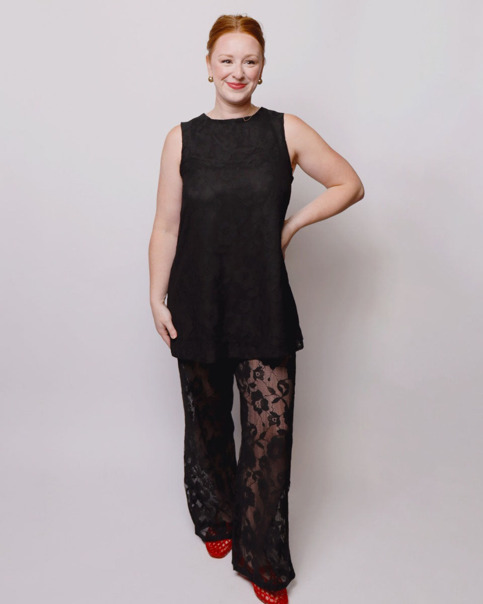 Woman wearing a black sleeveless top and black lace pants on a white background