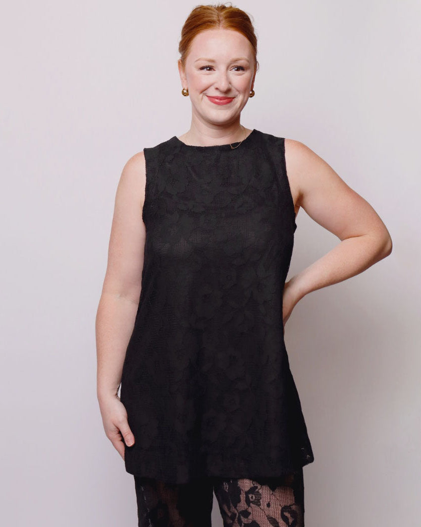 Woman wearing a black sleeveless top with lace details on a plain background