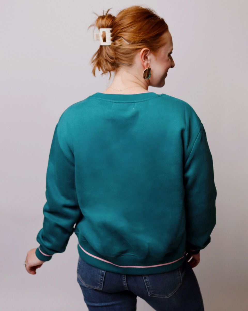 Person wearing a teal sweatshirt and blue jeans against a plain background