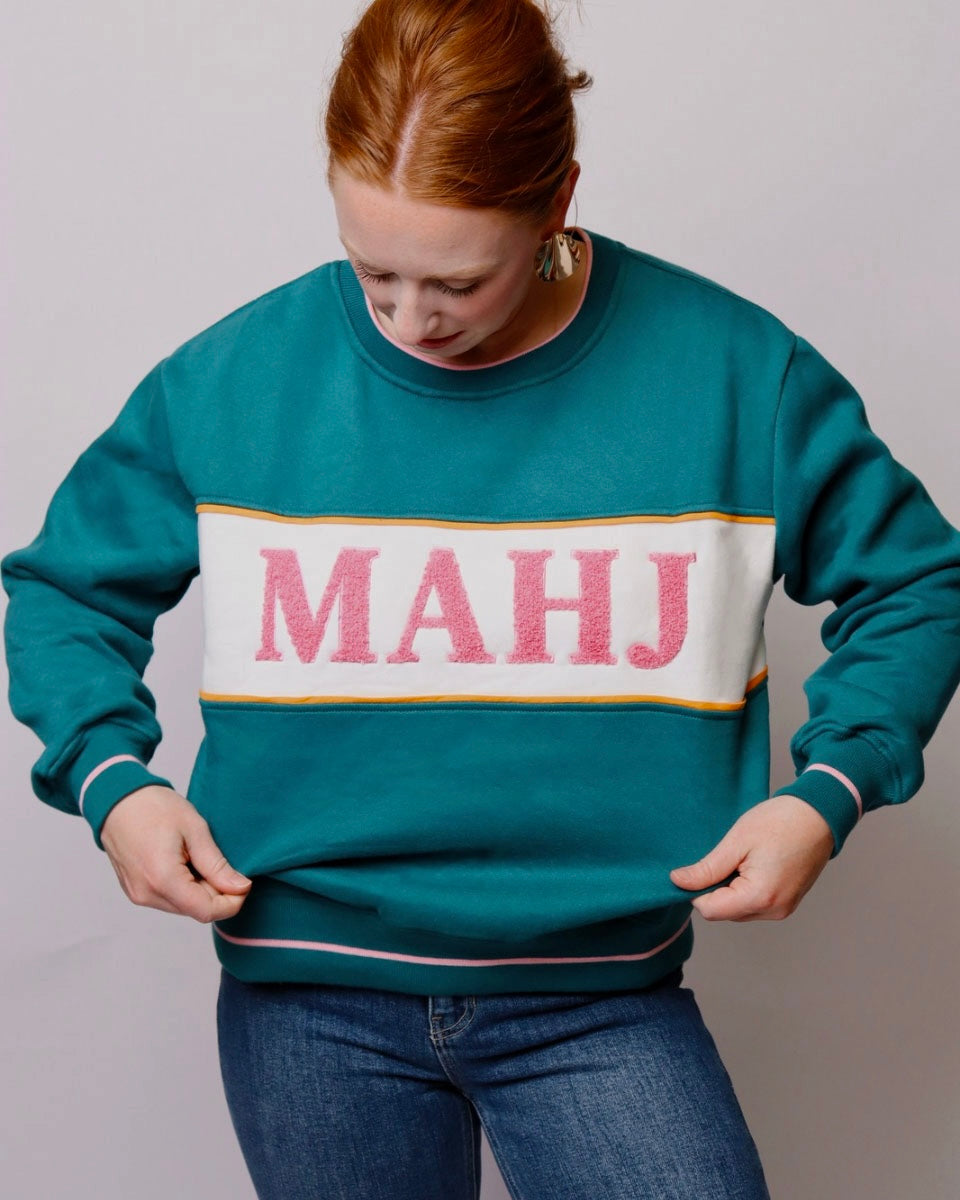 Person wearing a teal sweatshirt with 'MAHJ' printed on it against a plain background