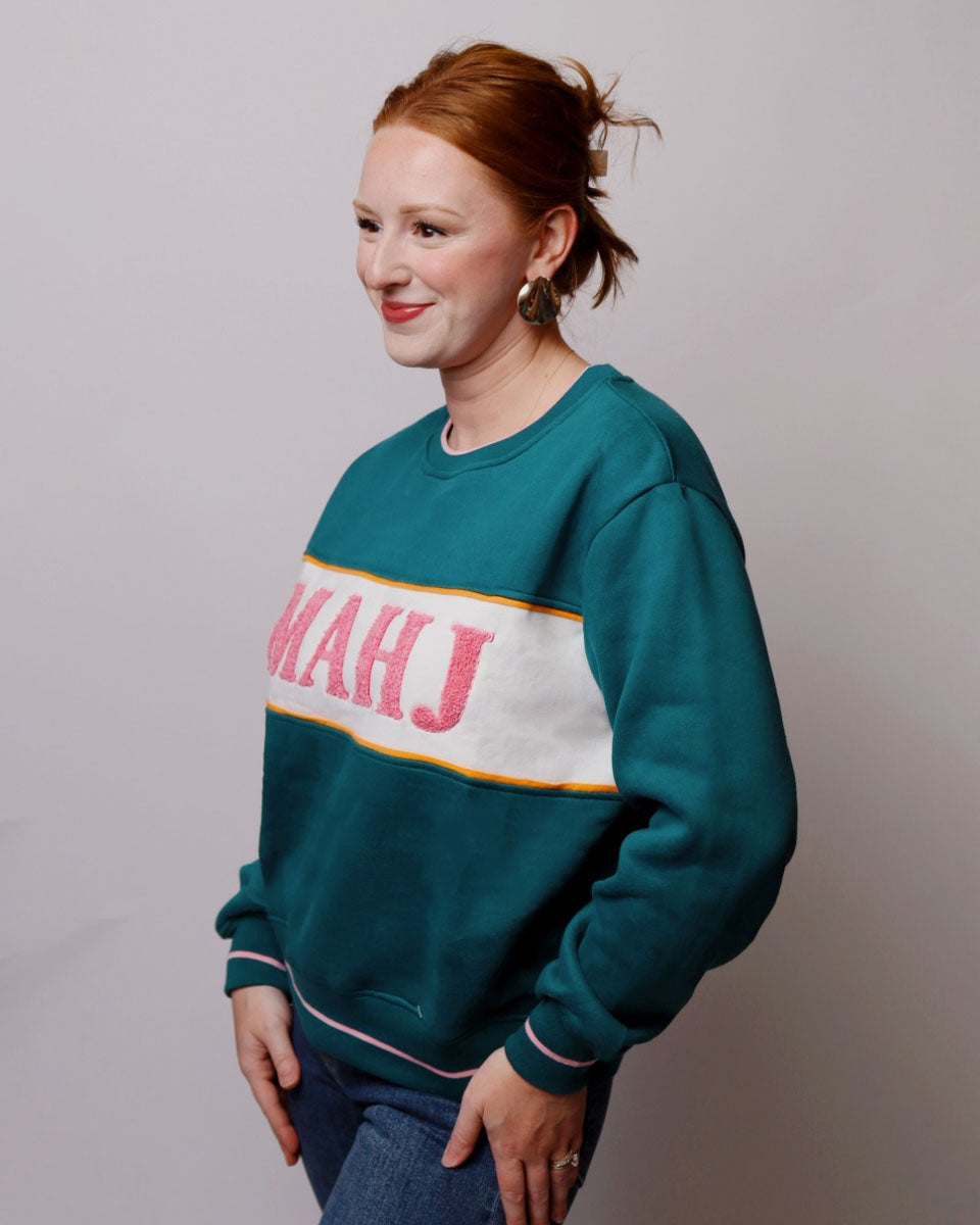 Person wearing a teal sweatshirt with colorful text on a plain background