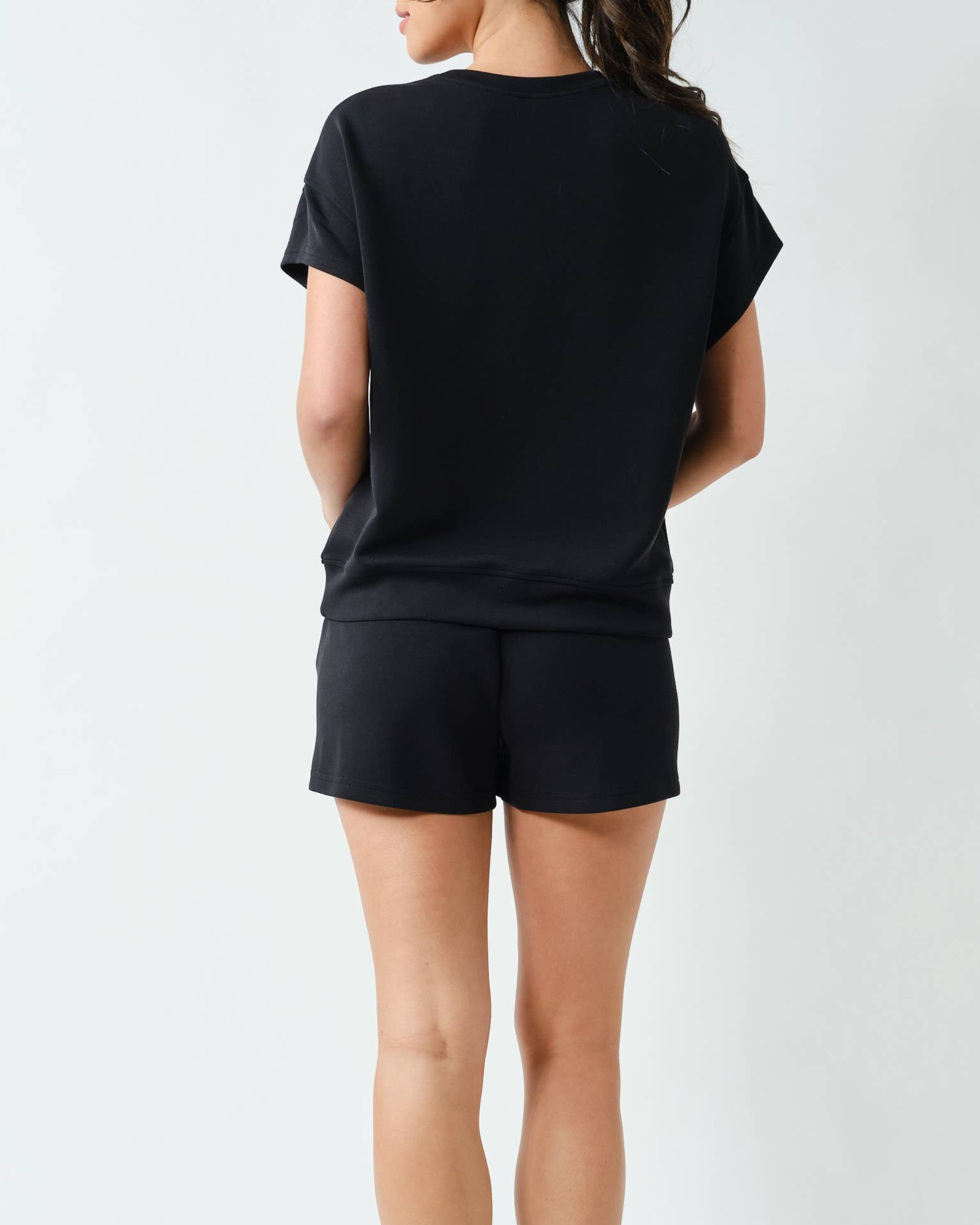 Model wearing a black shorts set outfit on a neutral background back view