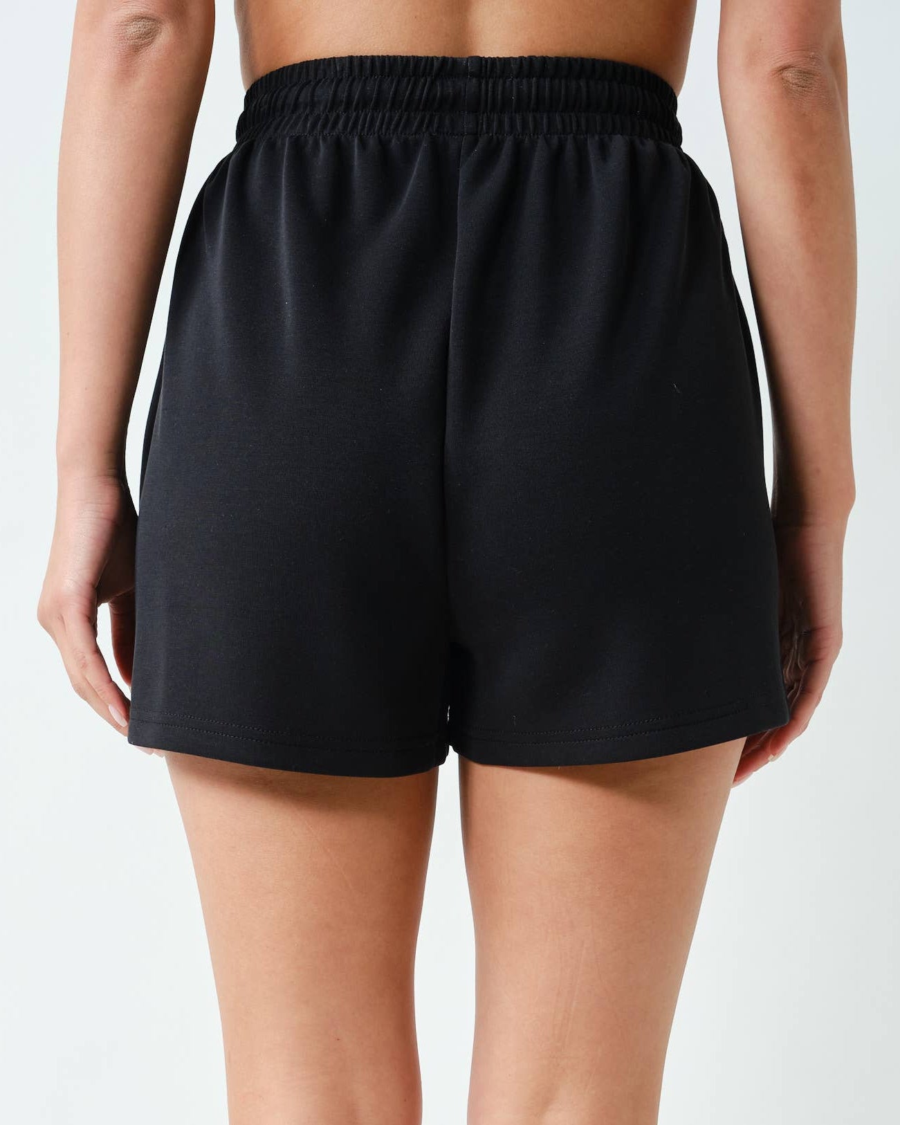 Model wearing a black shorts set outfit on a neutral background shorts back view