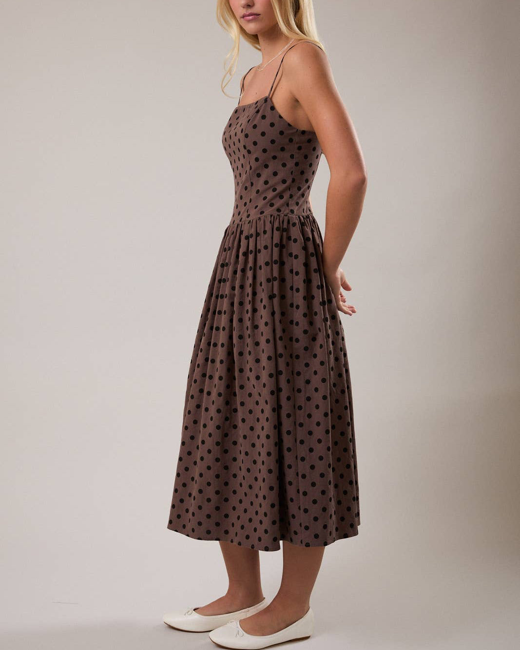 Woman wearing a brown polka dot dress against a plain background