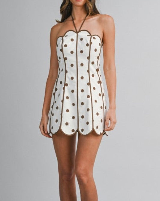 Model wearing a halter min dress with brown  polka dots on a neutral background