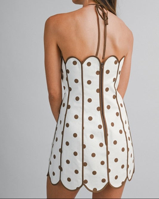 Model wearing a halter min dress with brown  polka dots on a neutral background back view