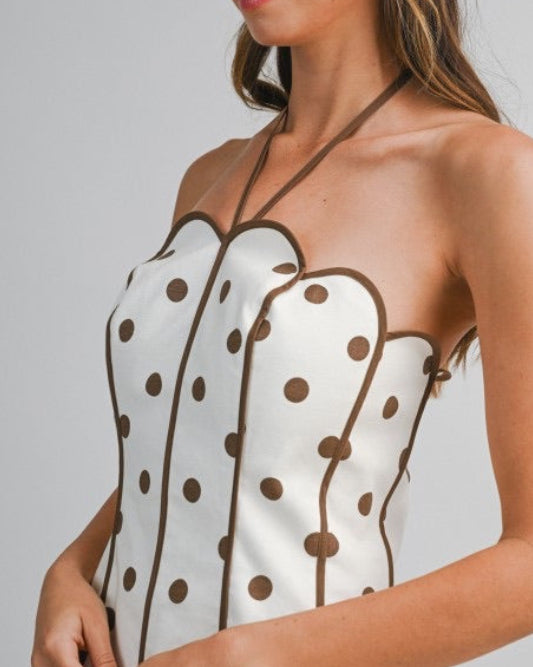 Model wearing a halter min dress with brown  polka dots on a neutral background xlose side view