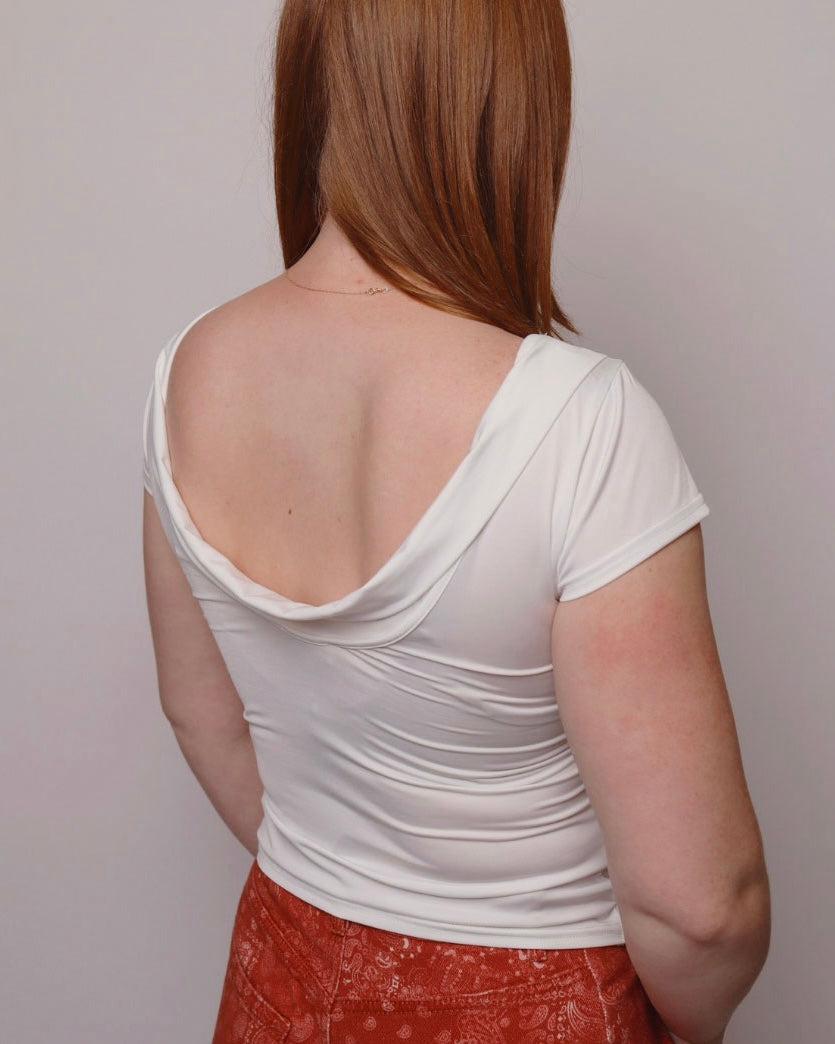 Person wearing a white open-back top and red pants against a plain background