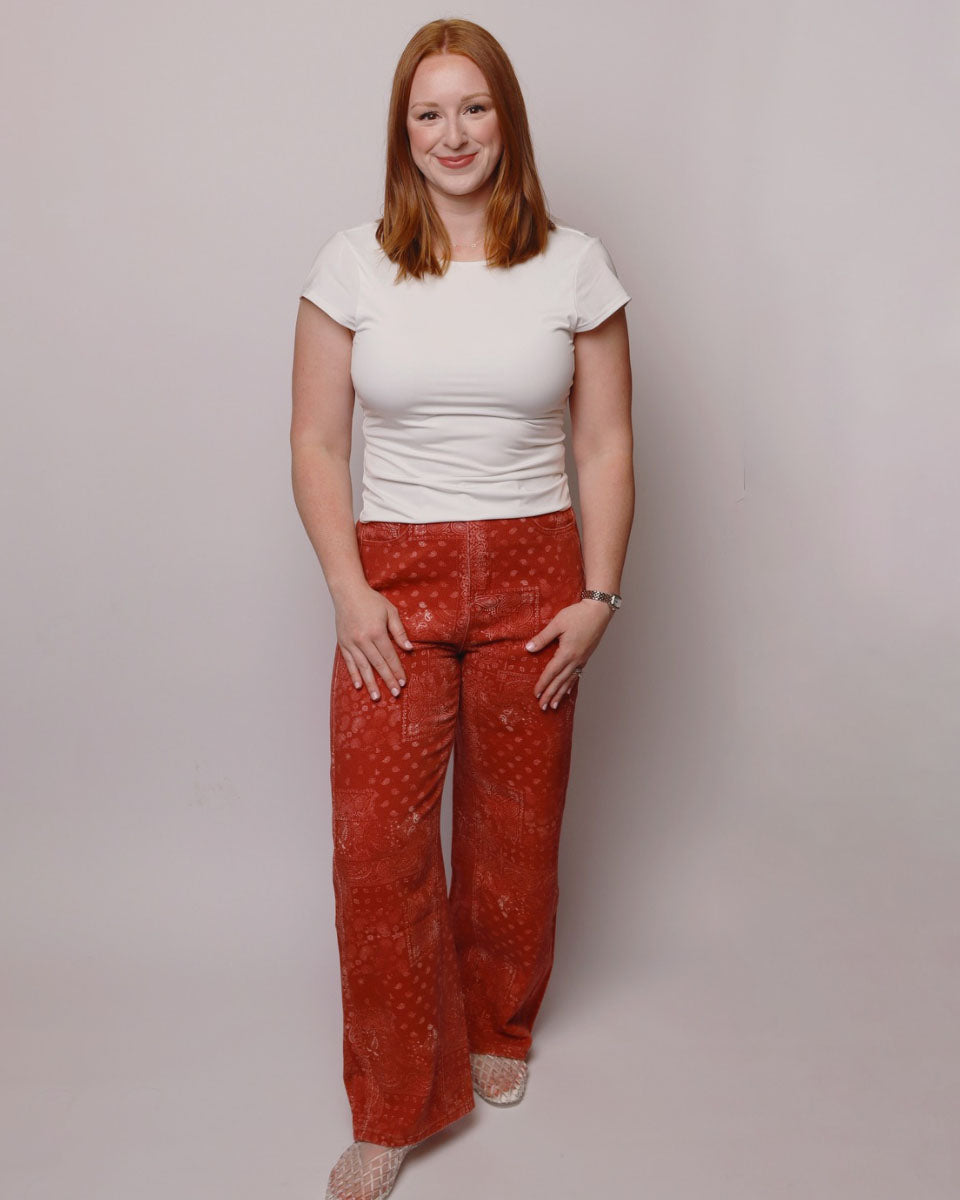 Woman wearing a white top and red patterned pants against a plain background