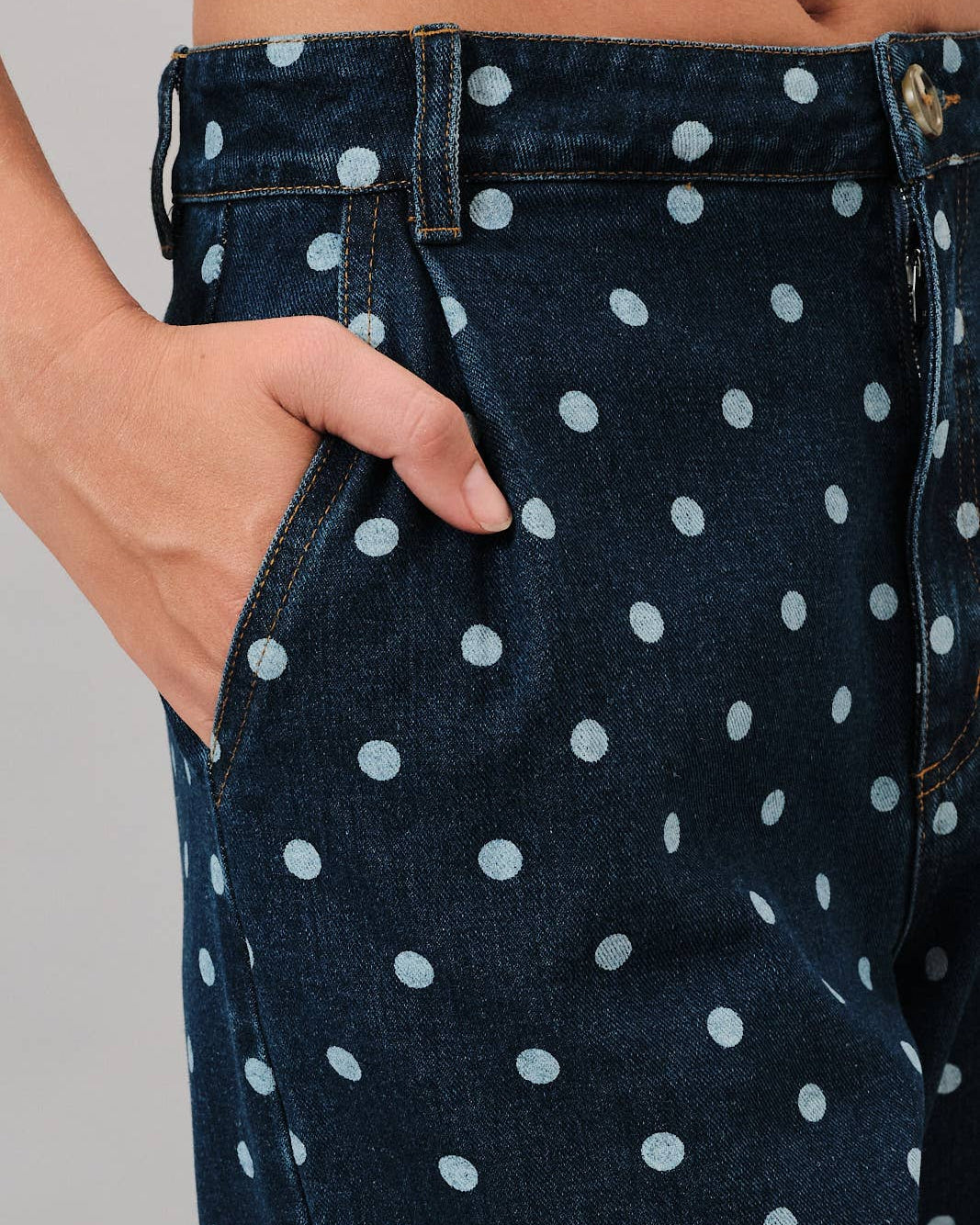 Navy blue jeans with white polka dots worn by a person on a gray background