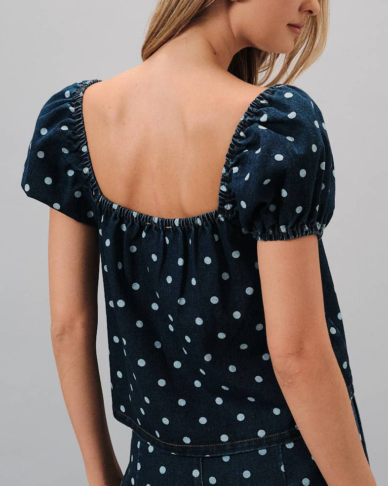 Woman wearing a navy blue polka dot dress against a gray background