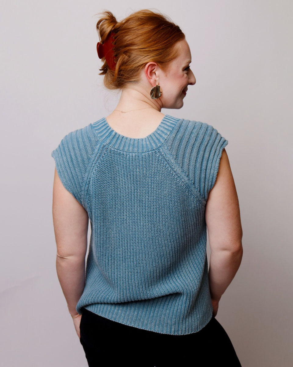 Woman wearing a blue knitted sleeveless sweater against a plain background