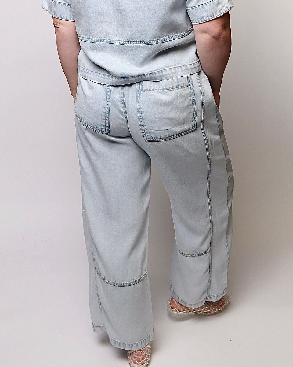 A person shown from the back wearing light-wash wide-leg denim jeans with a matching top, standing against a plain light gray studio background.