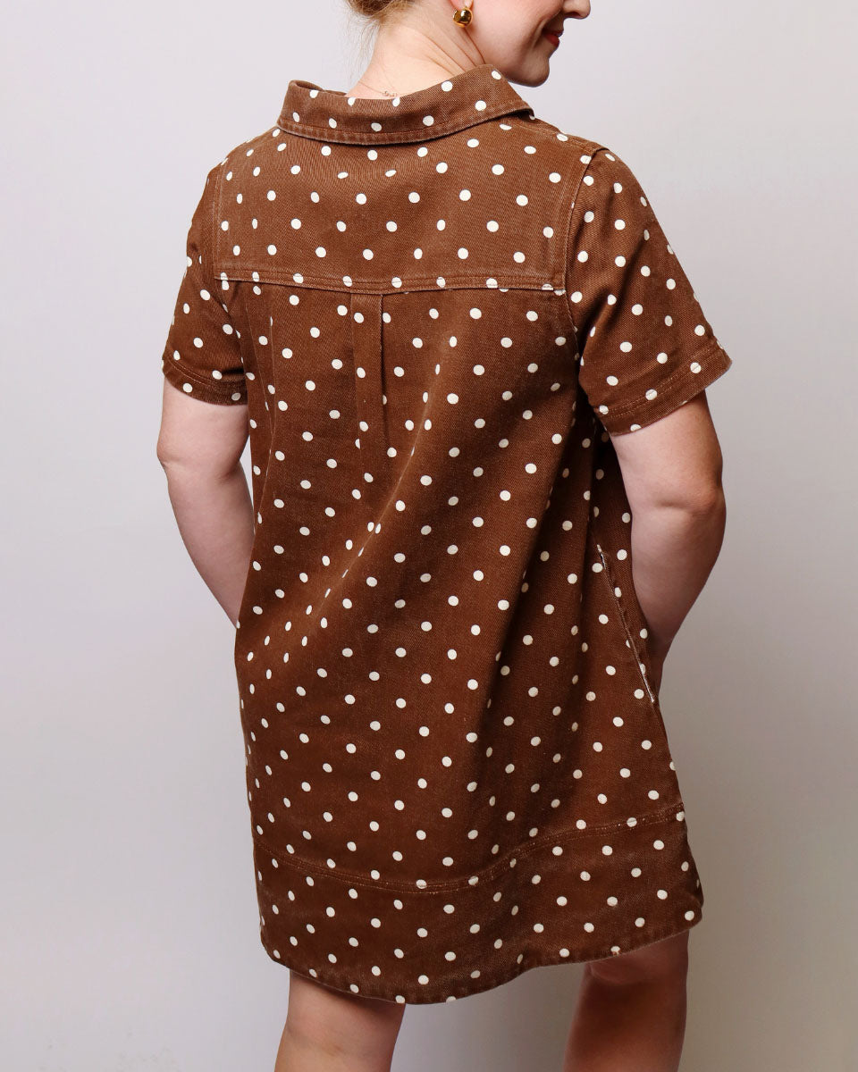 A woman wearing a brown short-sleeve collared dress with a white polka dot pattern, shown from the back against a plain light gray background.