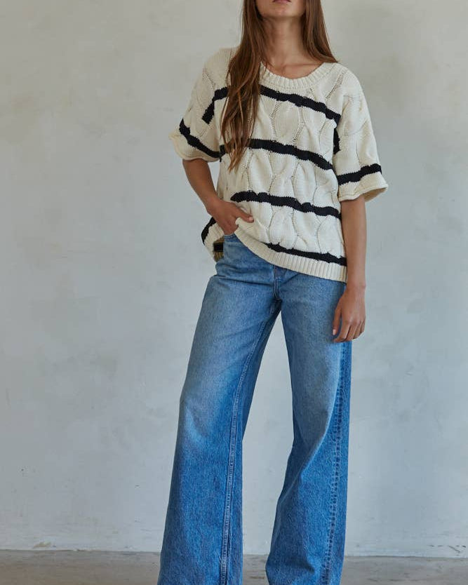 Woman wearing a striped sweater and blue jeans against a plain background