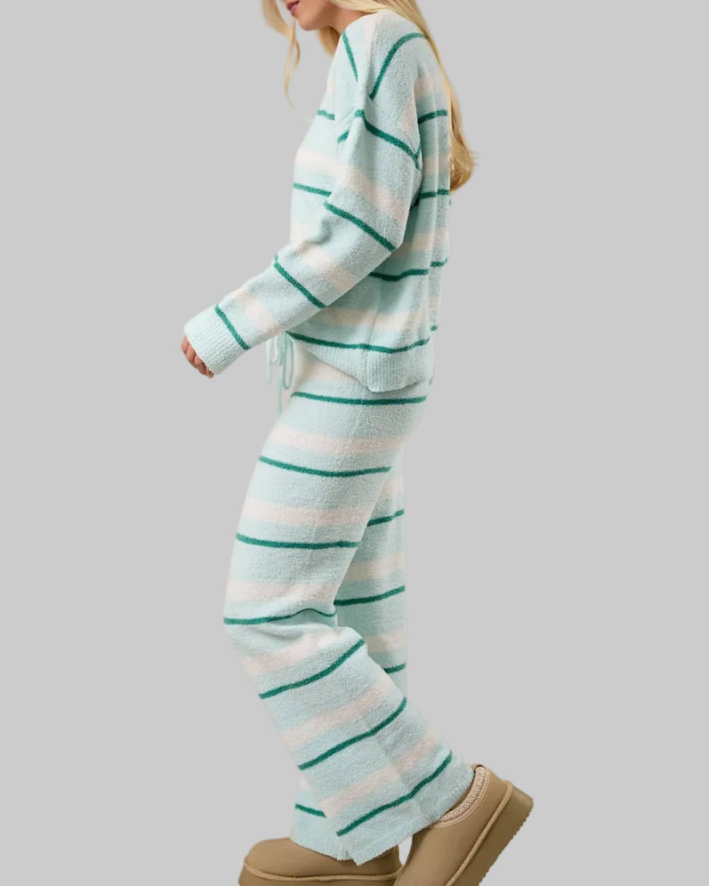 Woman wearing a light blue and white striped pajama set with beige slippers on a plain background
